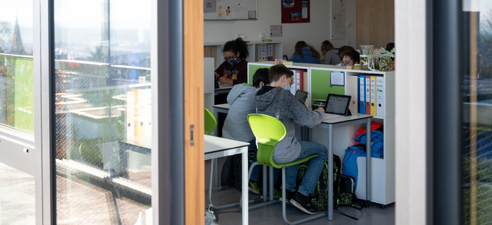 Schüler sitzen im Klassenraum und schreiben. Das Fenster ist geöffnet.